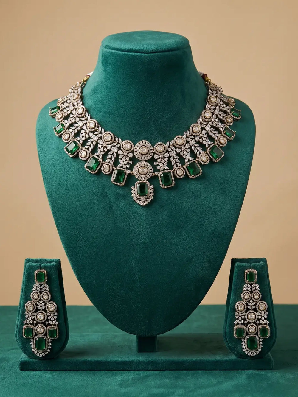 An ornate silver-toned jewelry set displayed on a teal velvet mannequin bust, including a wide collar necklace and two matching earrings, with green gemstone accents against a beige background.