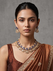 Woman wearing a blue floral Kundan necklace set with vibrant enamel accents, Polki and CZ stones, warm gold-plated detailing and matching earrings.