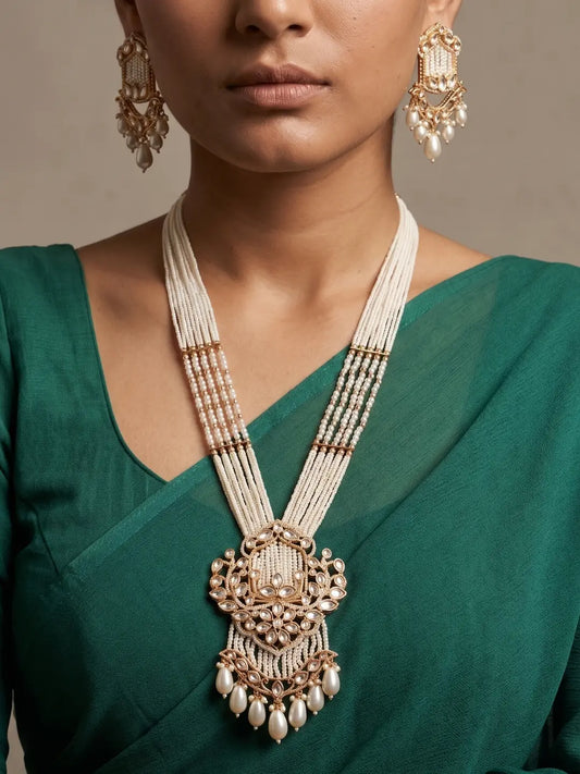 Woman wearing a long white Kundan pendant necklace with multiple pearl bead strands, floral-inspired detailing, a statement pendant, drop accents and matching earrings.