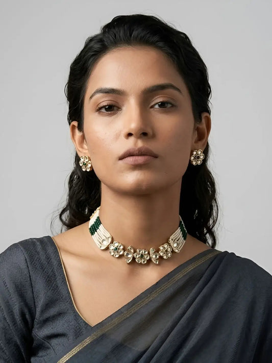 a women wearing delicate green stone kundan and pearl choker necklace set
