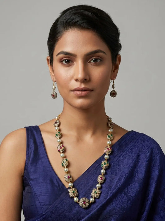 Woman wearing a handcrafted multicolour beaded necklace with antique metallic beads, green and ruby-red stone accents, shell pearl beads and matching drop earrings.