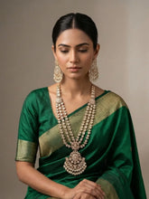 Woman wearing a green saree with a gold border and long layered polki necklace set with a bold pendant jewelry against a neutral background