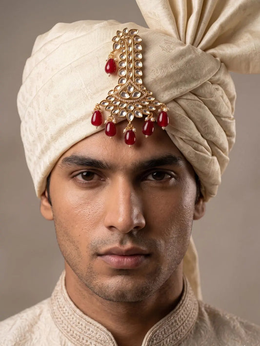 Groom wearing a red Polki Kundan kalangi styled on a traditional wedding safa.