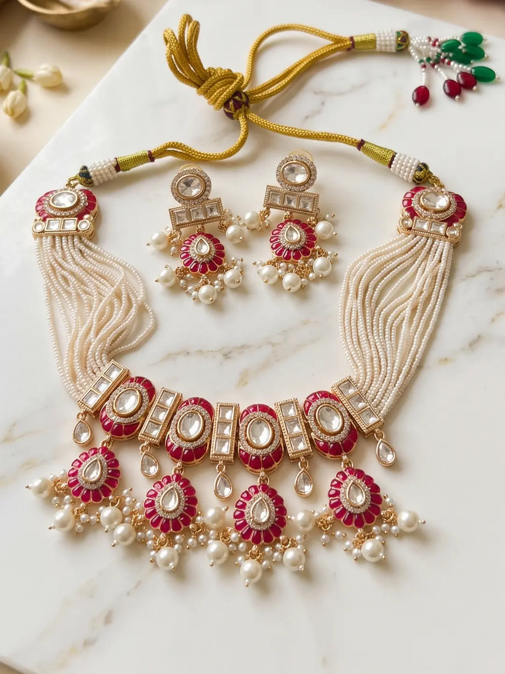 Flat lay showing a red Polki pearl choker necklace set with intricate Kundan-inspired detailing, red Meenakari accents, pearl strands and matching earrings.