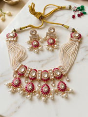 Flat lay showing a red Polki pearl choker necklace set with intricate Kundan-inspired detailing, red Meenakari accents, pearl strands and matching earrings.