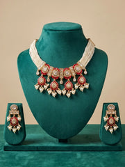 Red Polki pearl choker displayed on a green neck mannequin, highlighting the intricate stonework, pearl strands, red Meenakari accents and Kundan-inspired detailing.