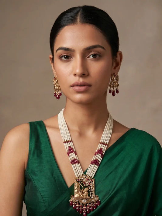 Woman styled in a red Ram Hanuman inspired temple necklace featuring layered pearl strands, devotional pendant artwork, Kundan-style white stones, pearl clusters and matching earrings.