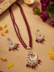 A traditional Indian jewelry set featuring a long beaded necklace and matching earrings. The necklace consists of deep red beads draped over a mother of pearl crescent pendant adorned with white polki stones and dangling red beads.