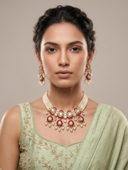 A woman wearing a traditional Indian jewelry choker set featuring a gold-plated necklace and matching earrings with red meenakari and white pearls, paired with a light green embroidered blouse.