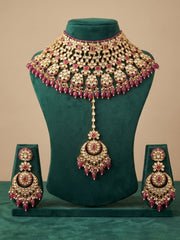 Ruby red Kundan bridal choker featuring floral motifs, stone detailing, matching maang tikka and chandelier earrings for bridal wear.