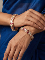 Close-up of hands wearing gold-plated bangles studded with polki kundan with red stones against a blue fabric background