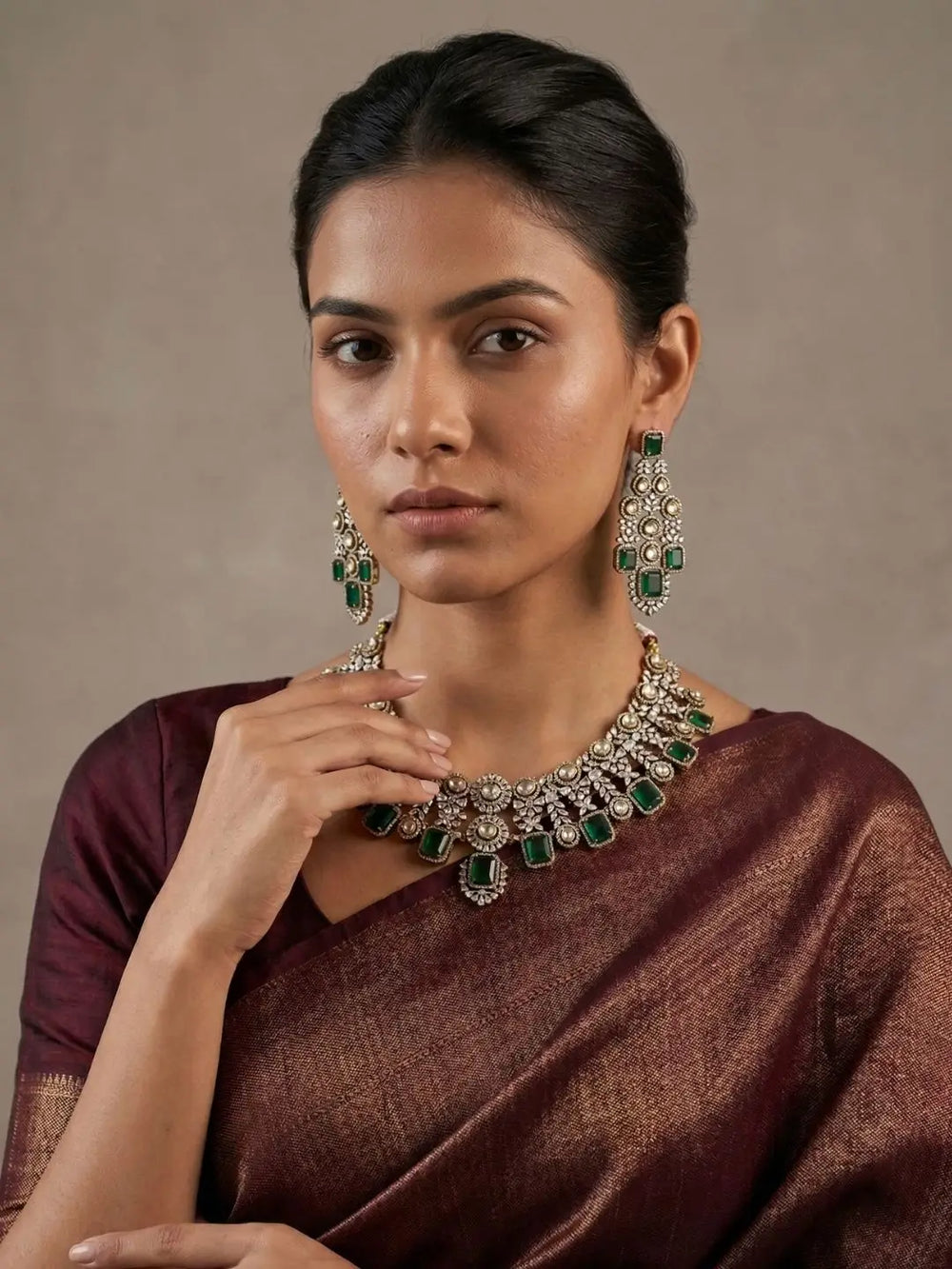 Woman wearing a brown saree with a prominent green emerald and cz stones necklace and earrings against a neutral background