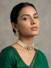 A woman wearing an ornate dual-toned polki choker necklace with pearl details and matching earrings, paired with a green blouse, against a neutral textured gray background.