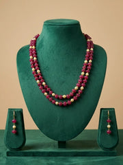 A dual-strand, ruby-red, watermelon-shaped beaded necklace and matching drop earrings displayed on a dark green velvet jewelry bust, set against a solid beige background.