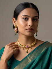 A woman wearing a traditional gold-plated antique jewelry set with pink and green stones, including a necklace and matching earrings, paired with a teal green saree.