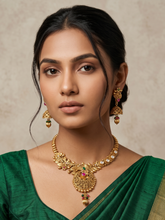 A woman wearing an ornate gold-toned traditional antique gold necklace with matching earrings and a green saree photographed against a soft beige textured background.