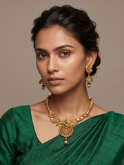 A woman wearing a green saree and traditional gold-plated antique jewelry , including a necklace with a large ornate pendant and matching drop earrings, against a plain beige background.