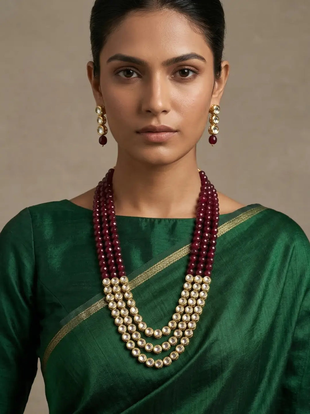 A woman wearing a dark green silk saree with a gold border and a multi-strand traditional Indian statement kundan layered necklace and matching earrings.