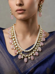 Woman wearing a pearl, kundan, and pink stone necklace with matching earrings against a neutral background