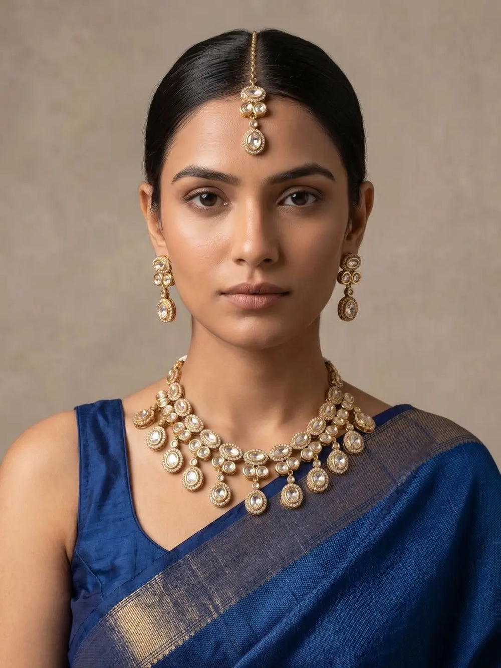 Woman wearing Gold Plated Polki Kundan Necklace Set With Tikka | Wedding & Festive Jewellery Set and a blue saree against a neutral background