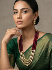 A woman wearing a green saree and a multi-strand beaded kundan necklace with deep red beads posed against a neutral studio background.