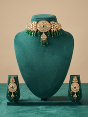 A traditional Indian choker jewelry set displayed on a dark teal velvet mannequin bust. The set includes a choker necklace with a large central oval motif, three side oval motifs, and dangling green bead fringes, along with matching earrings, all embellished with gold and clear stones.