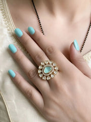 Hand wearing a polki ring with a mint green stone on a neutral background