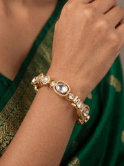 A rose gold-plated traditional Indian bangle bracelet with clear polki stones, worn on a person's wrist. The person is wearing a dark green saree with gold embroidery.