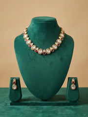 Gold-toned jewelry set displayed on a dark green velvet mannequin bust, featuring a necklace with round white stones and red gemstone accents, plus matching drop earrings on small standees below.