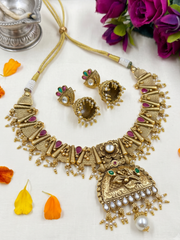 Gold-toned traditional Indian antique jewelry set featuring a statement necklace, matching earrings, and a small pendant, arranged on a light surface with decorative flower petals and flowers.