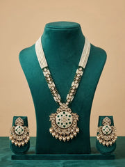 A traditional Indian jewelry set displayed on a dark teal velvet mannequin bust. The set includes a long necklace with a large ornate pendant, matching earrings, and a pair of bangles, all featuring white stones, green stones, and gold-toned metal.