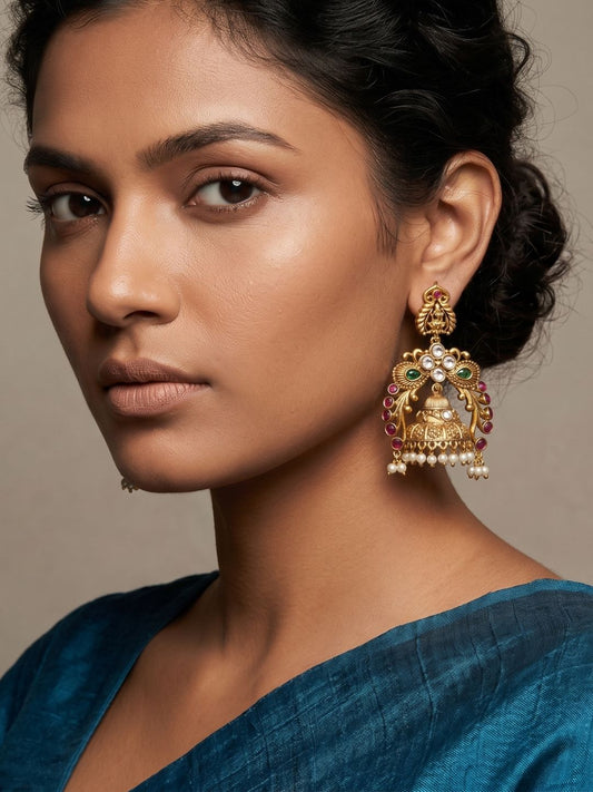 Gold plated antique Lakshmi Jhumka earrings with an intricate goddess motif, peacock-inspired design, colourful gemstones and pearl embellishments.