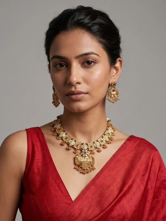 Antique gold-finish necklace featuring geometric detailing, red and green stones, pastel Meenakari and delicate ghunroo elements.