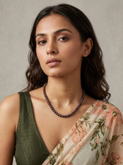 Single strand black freshwater pearl necklace with lustrous charcoal grey and iridescent beads laid out in a full curved view with gold-plated clasp
