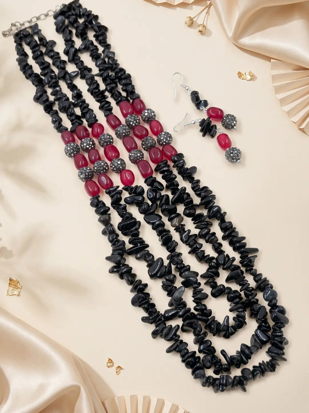 Multi strand black and red beaded necklace with drop earrings in a styled view, the fuller layered strands sitting around the neckline