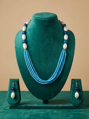 A jewelry set displayed on a dark green velvet mannequin bust, featuring a multi-strand necklace with light blue, dark blue, and white beads, along with matching drop earrings on small display stands against a solid beige background.