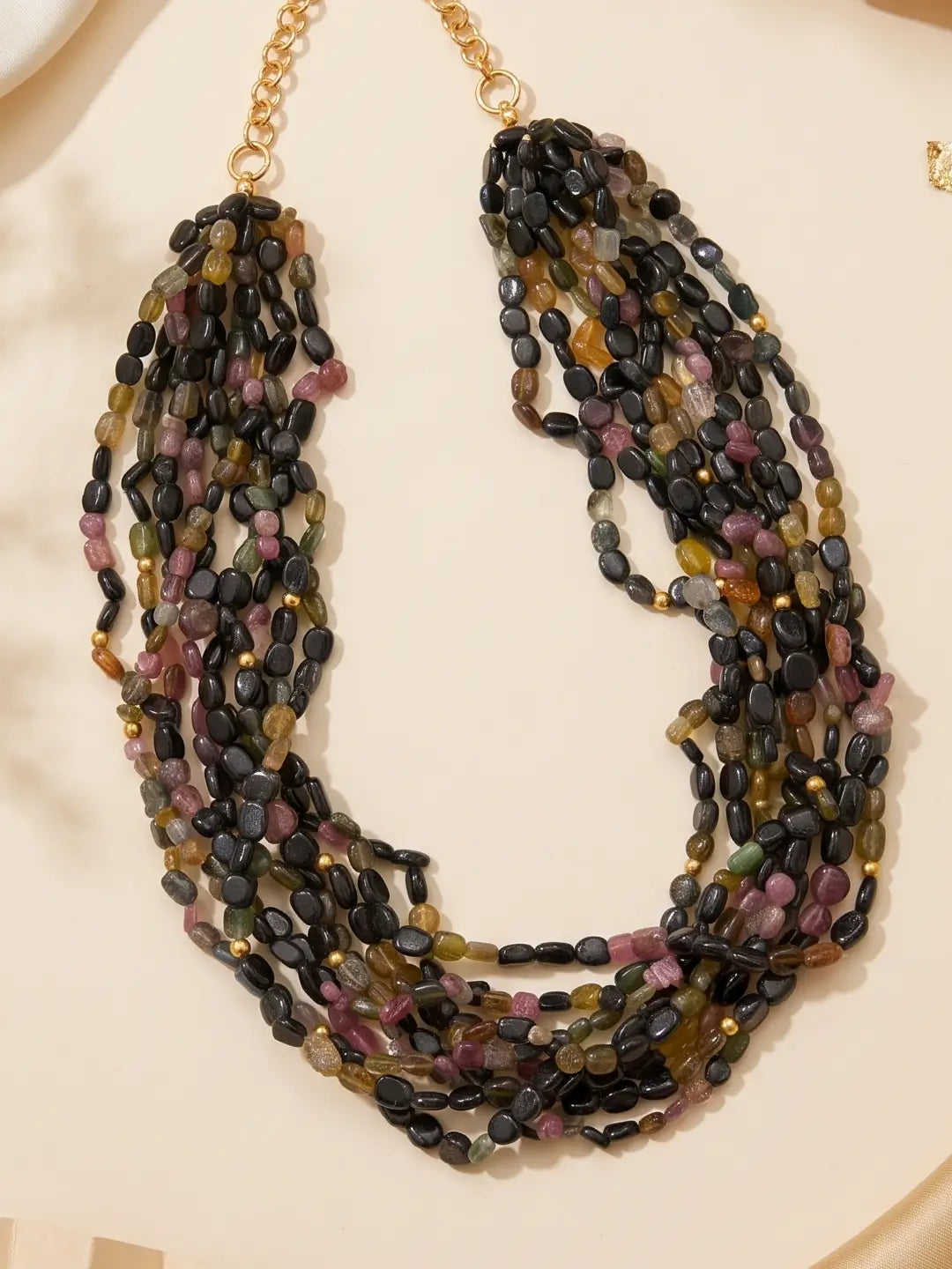 Styled view of a layered tourmaline beaded necklace with cascading strands in dark, green and pink shades, showing volume around the neckline