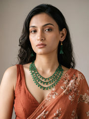 Close-up of small glossy green faceted beads and translucent green teardrop-shaped beads dangling along the cascading necklace strands

