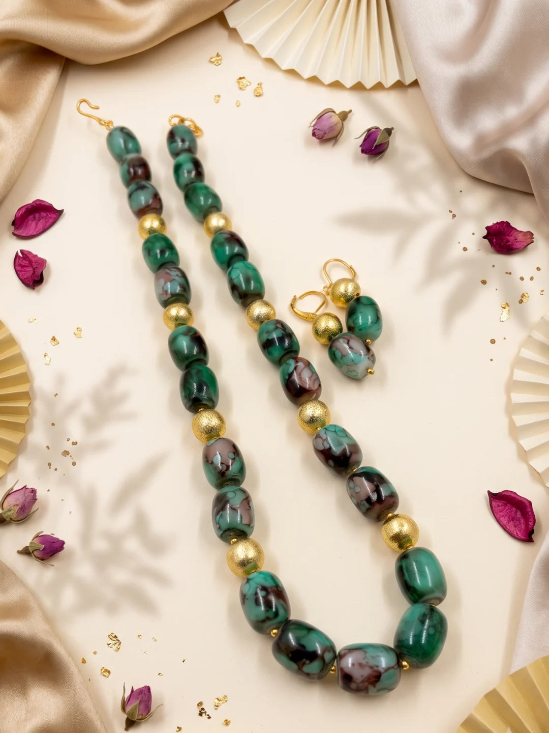 Close-up of green shaded chalcedony cylinder beads showing earthy colour variation, with small gold-plated round spacer beads between the stones