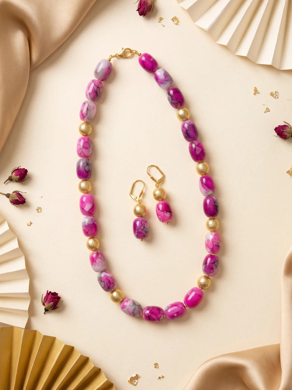 Close-up of pink shaded chalcedony cylinder beads arranged in a geometric pattern, separated by small gold-plated round spacer beads along the strands