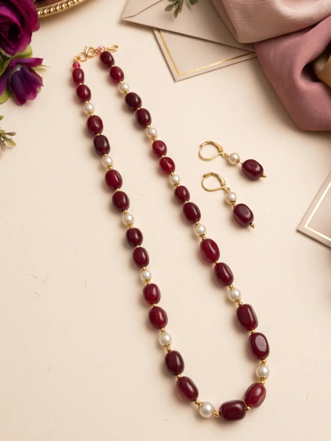 Close view of glossy red box-shaped jade beads alternating with faux pearls and gold-tone accents on a single-strand necklace