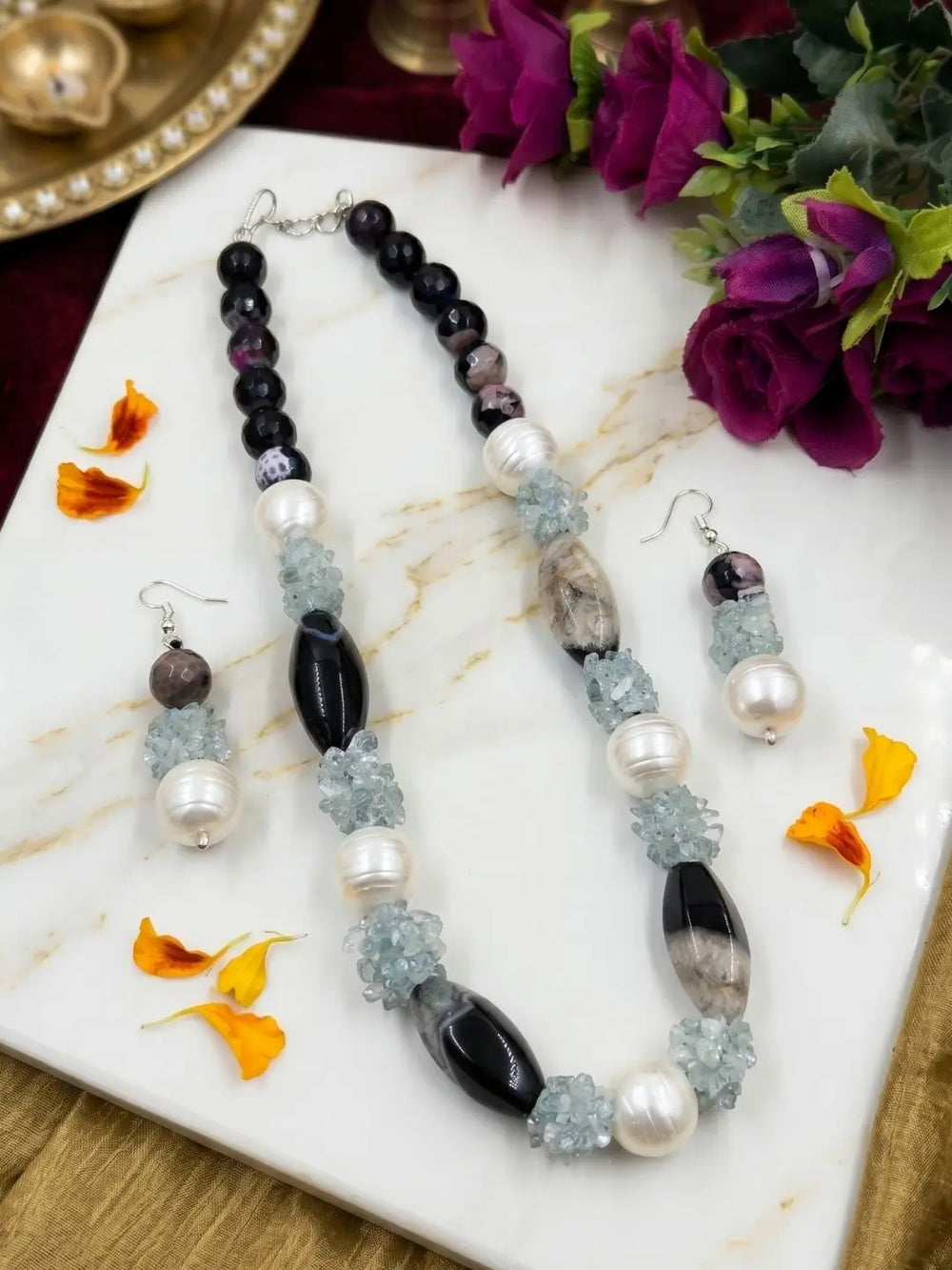 Close view of glossy round black onyx beads alternating with elongated black and grey beads, shell pearl accents and pale blue topaz chip clusters