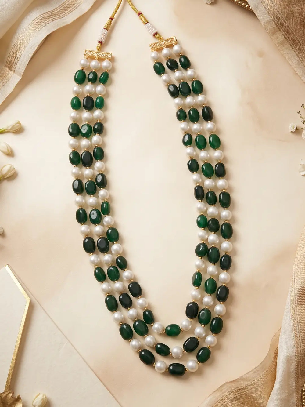 Close view of glossy green jade beads alternating with small white faux pearl beads across the layered strands of the mala