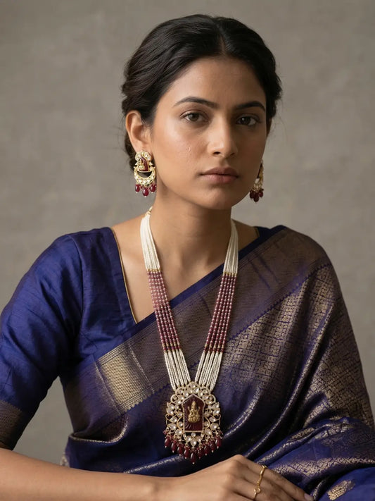 Woman wearing a long red Lakshmi Temple necklace set with multiple pearl bead strands, a detailed Lakshmi Devi pendant surrounded by Kundan Polki stones and matching earrings.