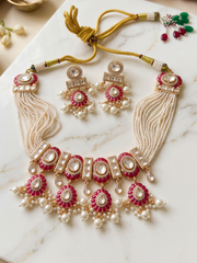 A traditional Indian jewelry set featuring a statement choker necklace and matching earrings, displayed on a white marble surface. The set includes a cream-colored beaded necklace with gold-plated borders, red enamel accents, and white pearl-like beads, accompanied by matching drop earrings.