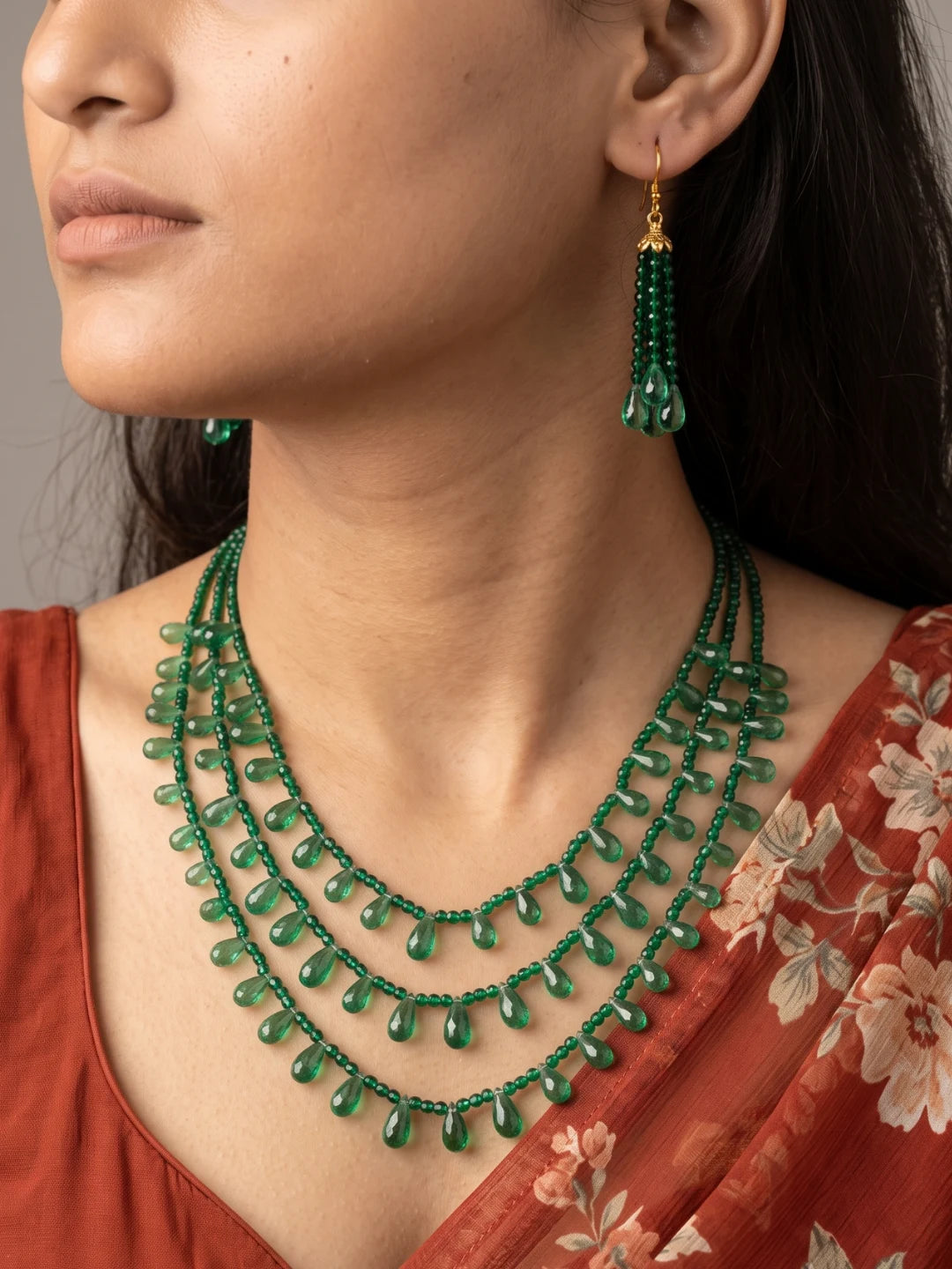 Full view of a layered emerald green necklace with glossy faceted beads and translucent teardrop accents, shown with matching drop earrings
