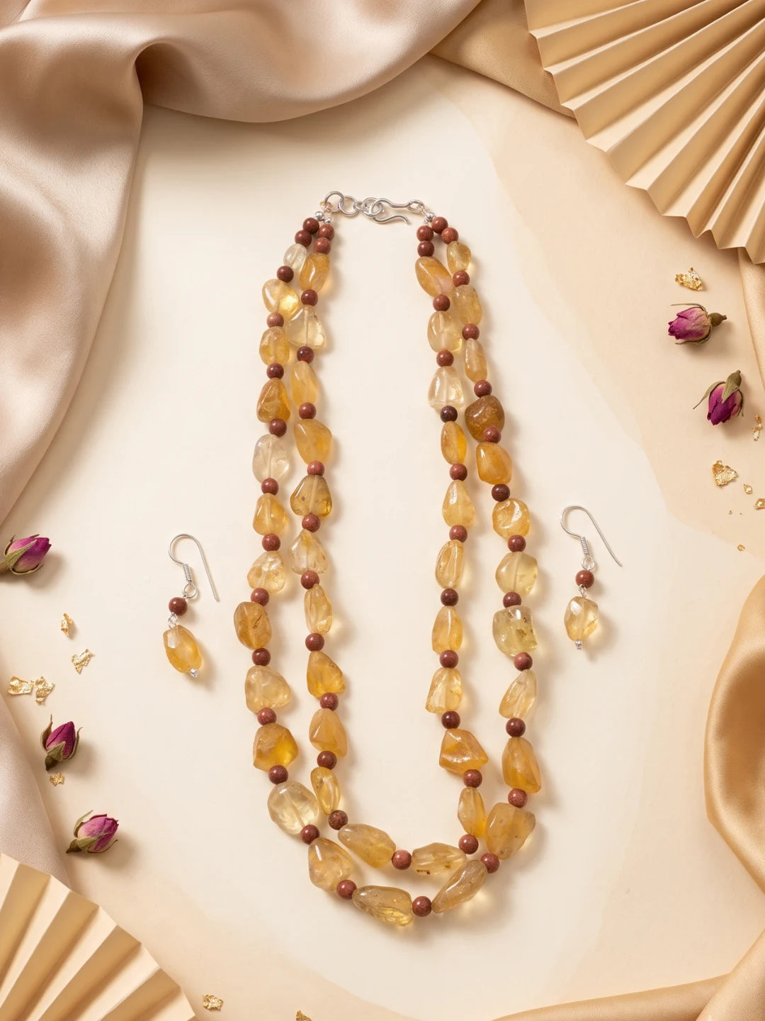 Flat lay of a double strand necklace with faceted yellow citrine and round tiger eye beads, silver-tone accents and a pair of matching drop earrings