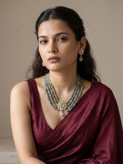 Close-up of a gold-plated floral Kundan pendant featuring a green cabochon-style centre stone and a pink teardrop accent.

