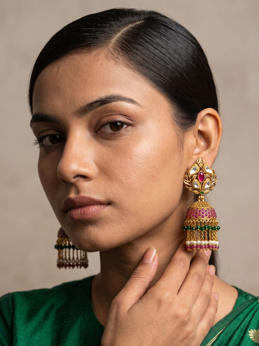 Gold-plated antique gold jhumka earrings featuring Kundan Polki stones, a ruby-pink centre and pearl and green bead embellishments
