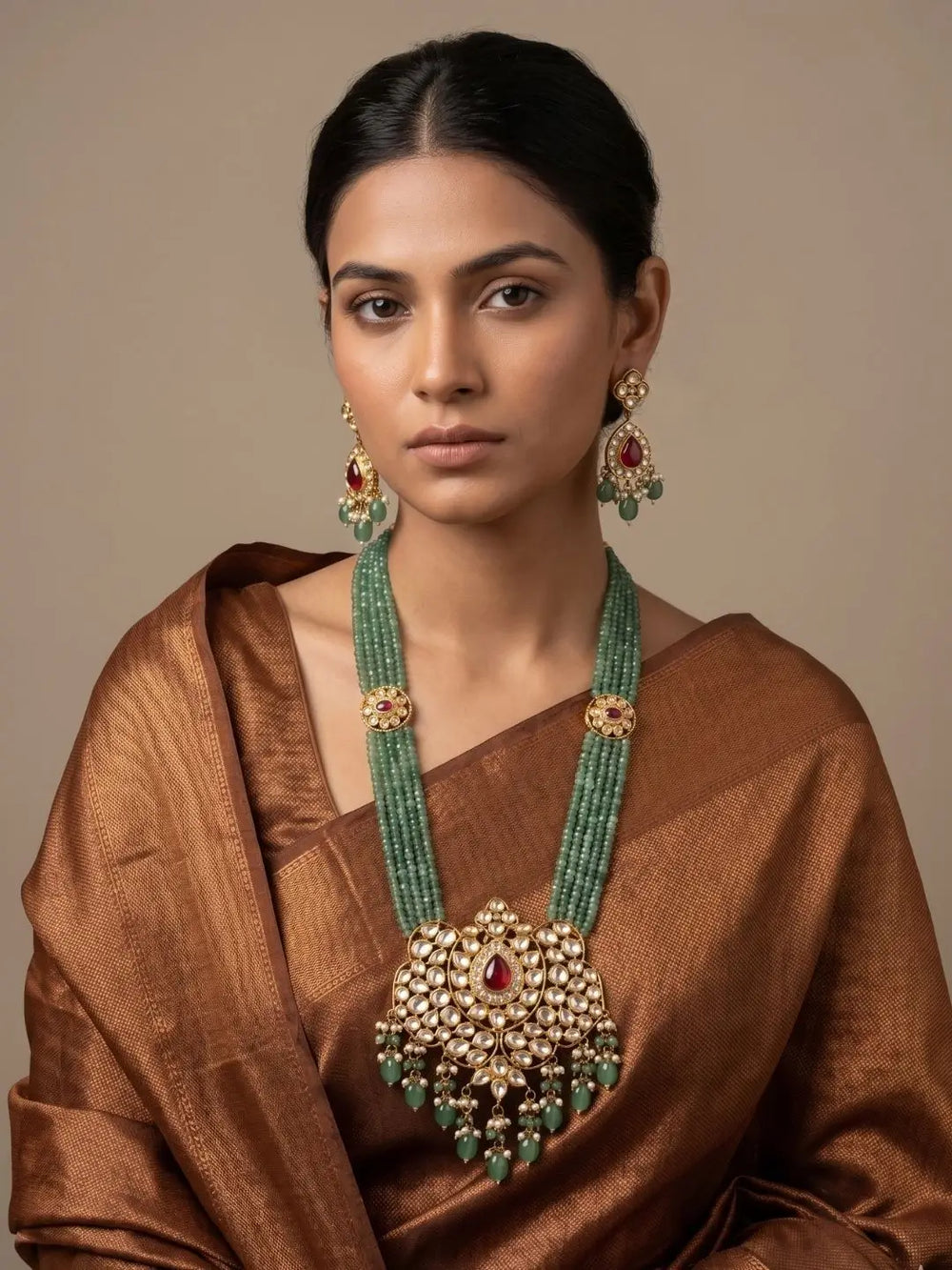 Matching jhumka-style earrings with ornate gold-plated craftsmanship that echoes the green kundan necklace, finished with a post and push back closure